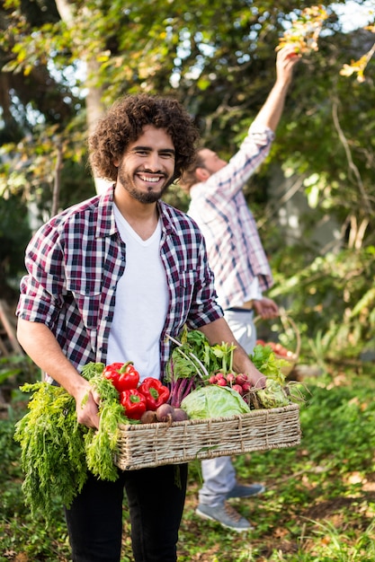 Portrait de jardinier hipster heureux avec des légumes et un collègue au jardin