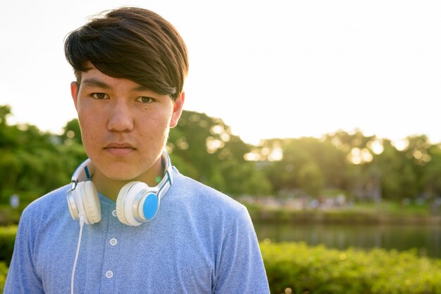 Portrait de jeune adolescent asiatique portant des écouteurs tout en vous relaxant dans le parc de Bangkok, Thaïlande