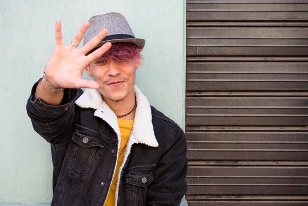 Portrait d'un jeune adolescent souriant et mettant sa main pour s'arrêter et se protéger Confidentialité et activité de protestation pour un beau garçon en plein air contre un mur Style de vie adolescent et concept rebelle