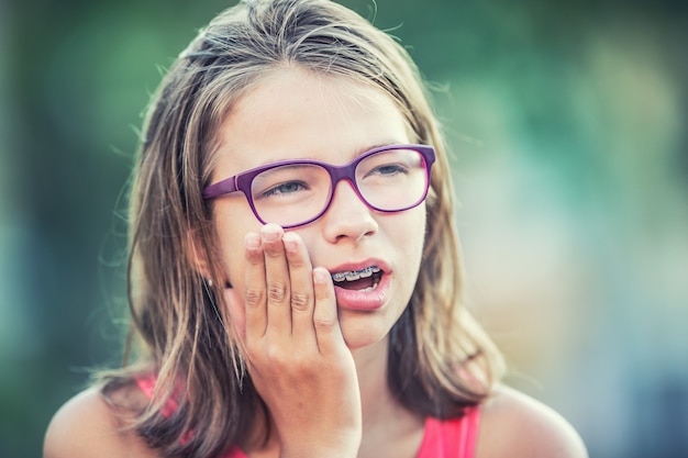 Portrait de jeune adolescente avec mal de dents. Fille avec des appareils dentaires et des lunettes.