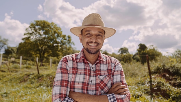 Portrait d'un jeune agriculteur avec les mains croisées dans la chemise décontractée et le chapeau à la ferme