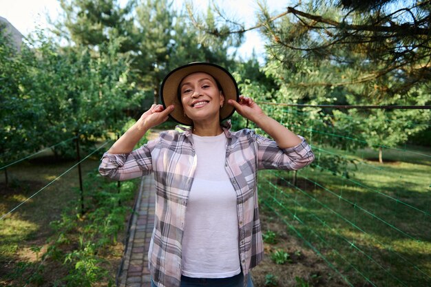 Portrait d'une jeune agricultrice gaie portant un chapeau de paille et appréciant le jardinage par une belle journée d'été ensoleillée