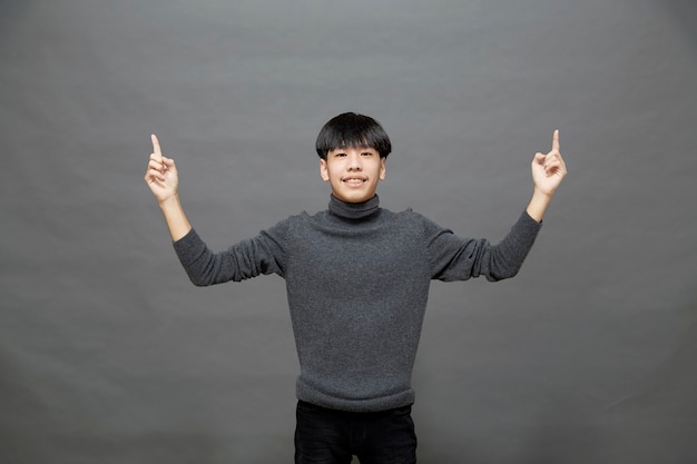 Portrait de jeune asiatique cheveux cool élégant portant un pull gris doigt pointé studio shot isolé sur fond gris