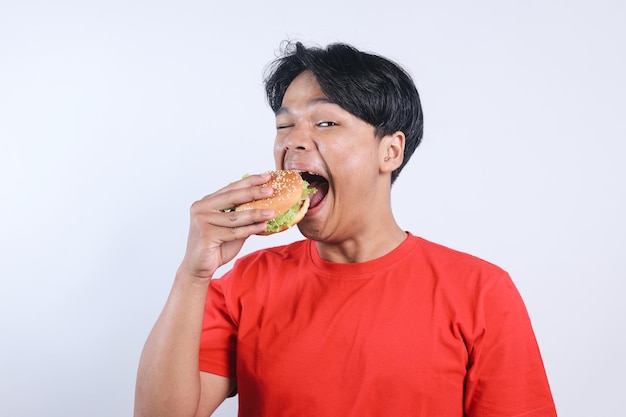 Portrait d'un jeune Asiatique excité mangeant un délicieux burger isolé sur un fond blanc