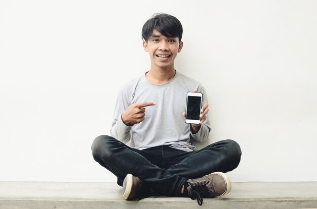 Portrait d'un jeune asiatique heureux pointant sur un téléphone portable