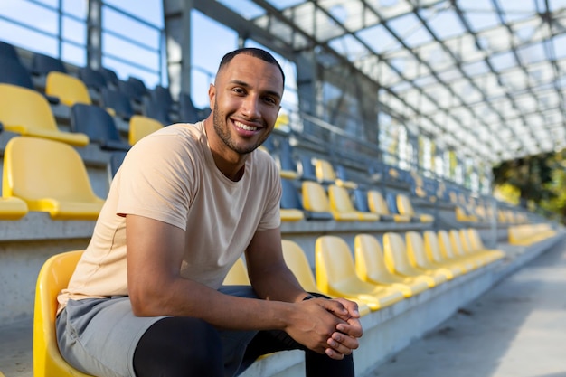 Portrait d'un jeune athlète dans un stade, un homme assis sur une chaise souriant et regardant la caméra de près.