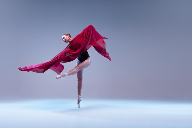 Photo portrait de jeune ballerine dansant avec un tissu transparent rouge foncé isolé sur un studio gris bleu