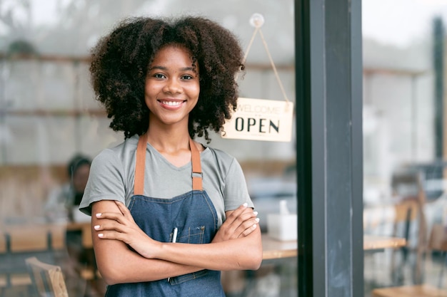 Photo portrait d'une jeune barista afro-américaine souriante debout avec les bras croisés dans son magasin