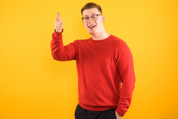 Portrait de jeune beau mec souriant en pull rouge montrant le geste sur jaune