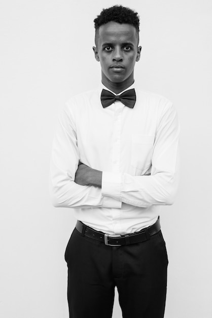 Portrait de jeune bel homme d'affaires africain avec noeud papillon contre un mur blanc en noir et blanc