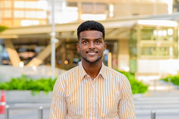 Portrait de jeune bel homme d'affaires africain souriant en ville