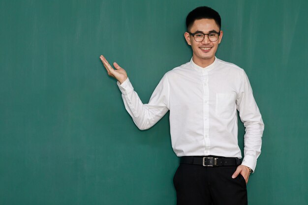 Portrait d'un jeune et bel homme asiatique portant des lunettes et des vêtements d'affaires décontractés, une chemise blanche et un pantalon noir, pose dans des gestes de publicité et présente des choses avec confiance en soi.