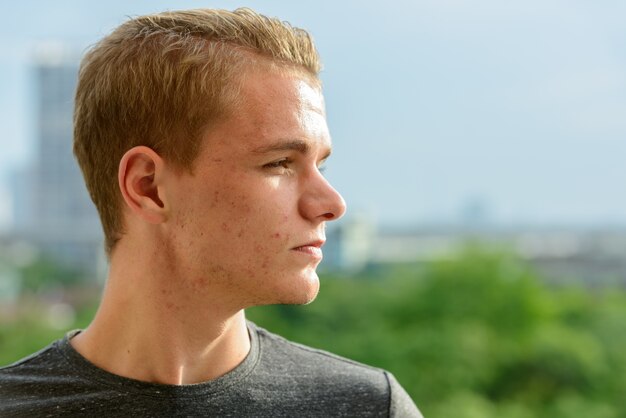 Portrait de jeune bel homme aux cheveux blonds contre vue sur la ville