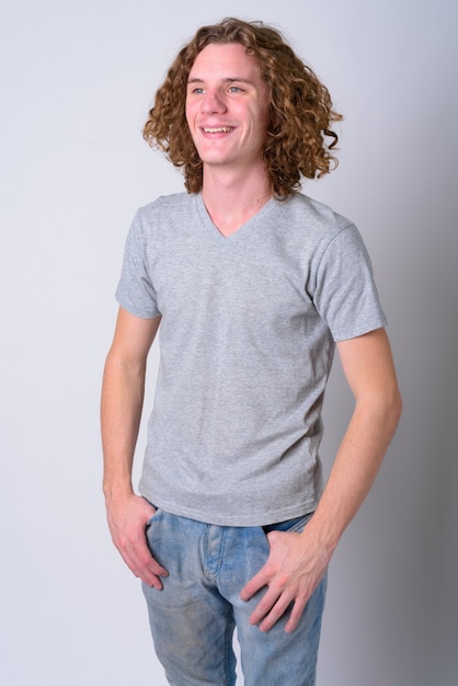 Portrait de jeune bel homme aux longs cheveux bouclés contre le mur blanc