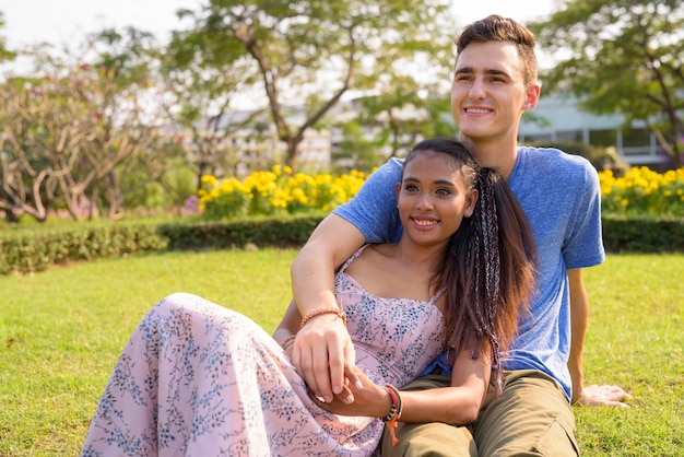 Portrait de jeune bel homme et belle jeune femme asiatique se détendre ensemble dans le parc