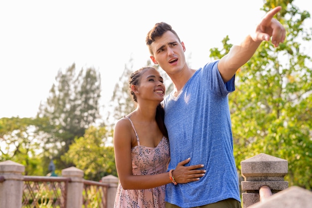 Portrait de jeune bel homme et belle jeune femme asiatique se détendre ensemble dans le parc