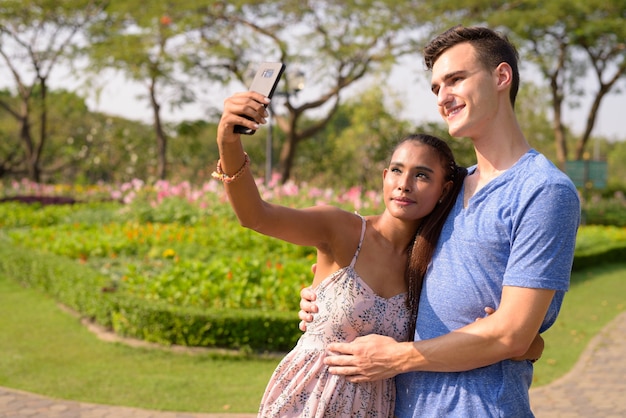 Portrait de jeune bel homme et belle jeune femme asiatique se détendre ensemble dans le parc