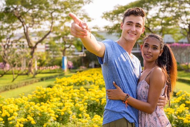 Portrait de jeune bel homme et belle jeune femme asiatique se détendre ensemble dans le parc