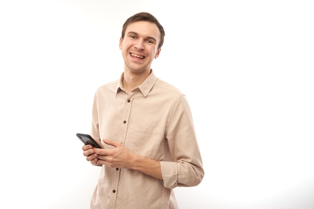 Portrait de jeune bel homme caucasien à l'aide de téléphone portable et souriant isolé sur fond de studio blanc expression faciale joyeuse