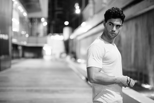 Portrait de jeune bel homme hispanique explorant les rues de la ville pendant la nuit