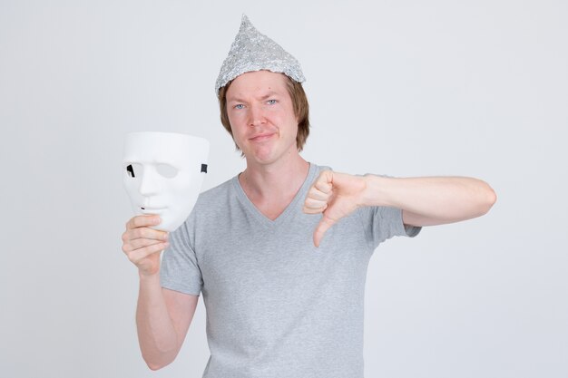Portrait de jeune bel homme portant chapeau de papier d'aluminium comme concept de théorie du complot sur blanc