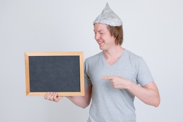 Portrait de jeune bel homme portant chapeau de papier d'aluminium comme concept de théorie du complot sur blanc