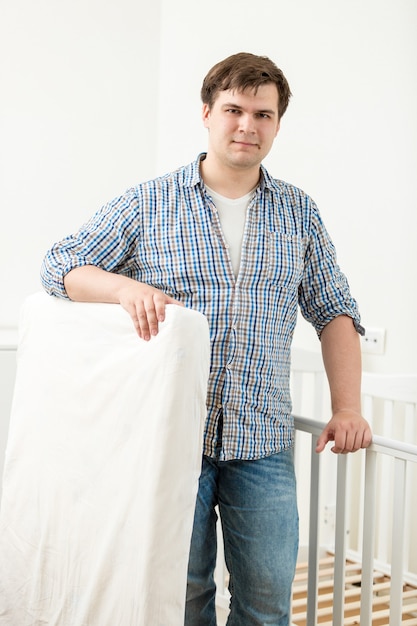 Portrait de jeune bel homme posant au lit de bébé avec un nouveau matelas