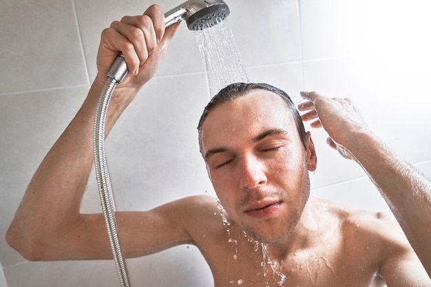 Portrait de jeune bel homme se lave avec du gel douche, mousse la tête avec du shampoing dans la salle de bain à la maison en gros plan