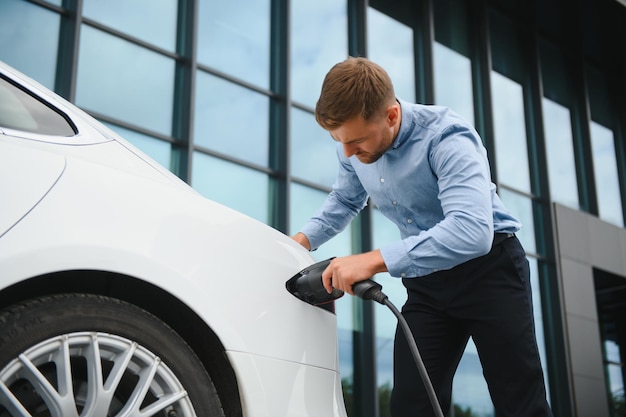 Portrait de jeune bel homme en tenue décontractée debout à la station de charge Concept de voiture électrique Eco