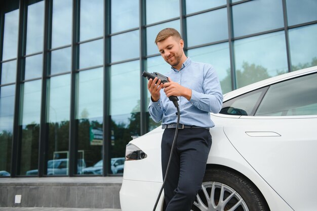 Portrait de jeune bel homme en tenue décontractée debout à la station de charge Concept de voiture électrique Eco