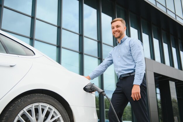 Portrait de jeune bel homme en tenue décontractée debout à la station de charge Concept de voiture électrique Eco