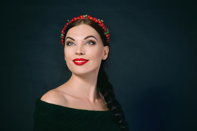 portrait de jeune belle brune souriante avec couronne rouge et tresse sur fond sombre