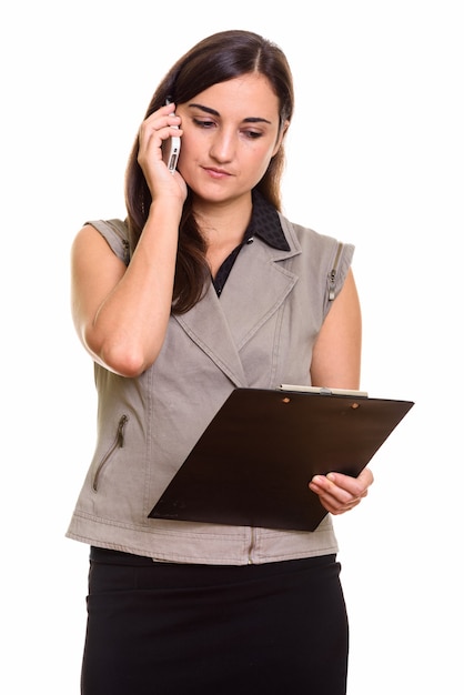 Portrait de jeune belle femme d'affaires à l'aide de téléphone tout en tenant le presse-papiers