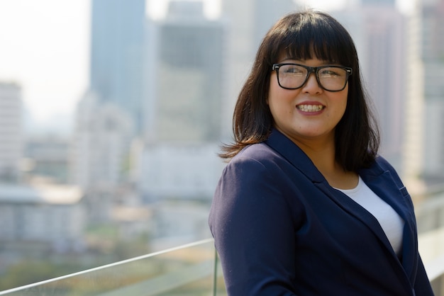 Portrait de jeune belle femme d'affaires asiatique en surpoids contre vue sur la ville