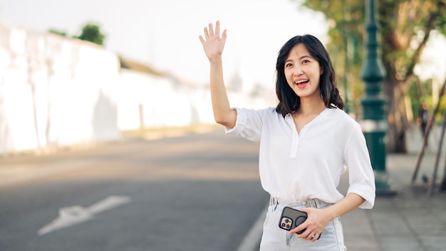 Portrait jeune belle femme asiatique agitant la main à un ami par la rue en vacances ensoleillées