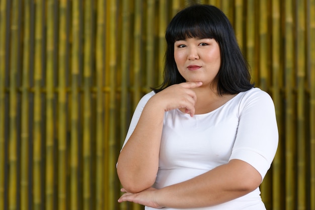 Portrait de jeune belle femme asiatique en surpoids contre le mur de bambou à l'extérieur