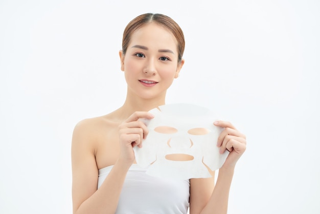 Portrait de jeune belle femme asiatique tenant un masque facial isolé sur fond blanc.