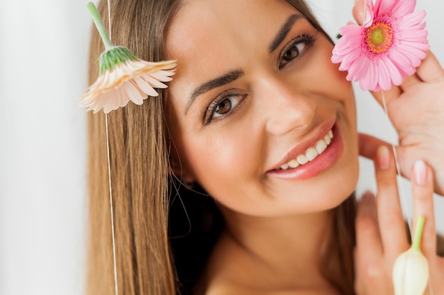 Portrait de jeune belle femme aux yeux bruns aux cheveux longs avec gerbera rose sur fond blanc Vacances de printemps Fête des mères