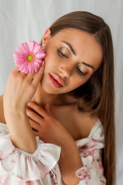 Portrait de jeune belle femme aux yeux bruns aux cheveux longs avec gerbera rose sur fond blanc Vacances de printemps Fête des mères