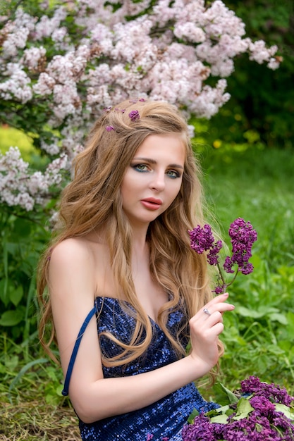 Portrait de jeune belle femme blonde posant parmi la floraison lilas.