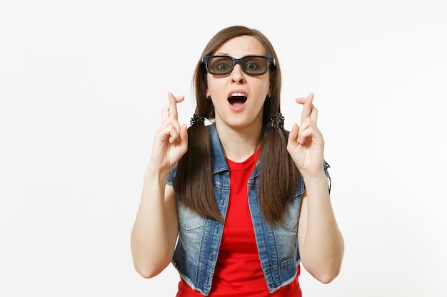 Portrait de jeune belle femme concernée dans des lunettes imax 3d et des vêtements décontractés en regardant un film et en gardant les doigts croisés isolés en studio sur fond blanc. Émotions dans le concept de cinéma.