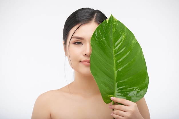 Portrait de jeune belle femme couvrant la moitié de son visage avec de grandes feuilles luxuriantes