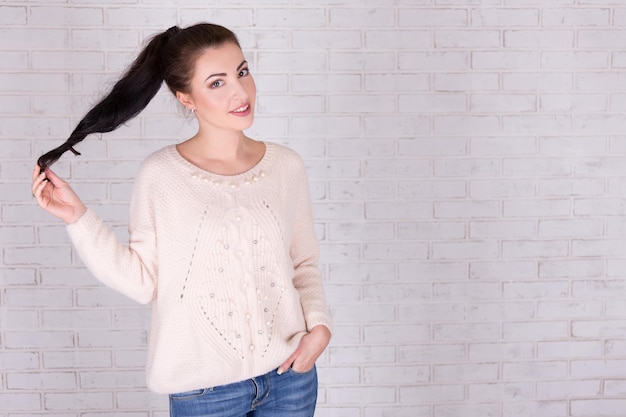 Portrait de jeune belle femme jouant avec ses cheveux et l'espace sur le mur de briques blanches