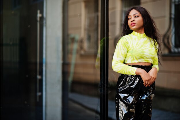 Portrait de jeune belle femme mannequin afro-américaine, porter en haut vert et pantalon noir brillant aspect mouillé.