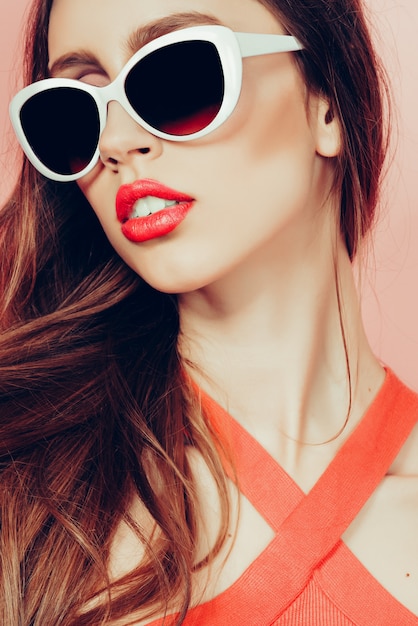 Portrait de jeune belle femme mince en robe sexy avec des lèvres sensuelles, lunettes de soleil. souriant et posant