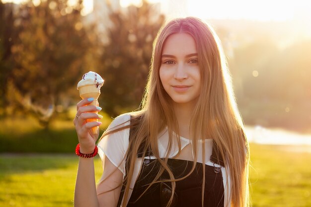 Portrait d'une jeune et belle femme peau fraîche et maquillage de beaux yeux mangeant de la crème glacée dans une corne de gaufre sur fond de parc