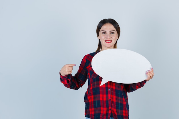 Portrait de jeune belle femme pointant sur bulle en chemise décontractée, jeans et à la vue de face joyeuse