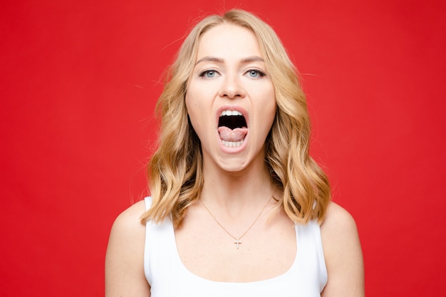 Portrait de jeune belle femme de race blanche avec des cheveux ondulés blond moyen et maquillage nu en t-shirt blanc hurlant de colère