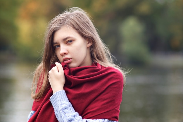 Portrait de jeune belle femme romantique sérieuse, fille adolescente en pull confortable et écharpe debout à l'extérieur en automne parc près du lac