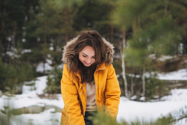 Portrait de jeune belle femme souriante en veste jaune marchant dans la forêt d'hiver